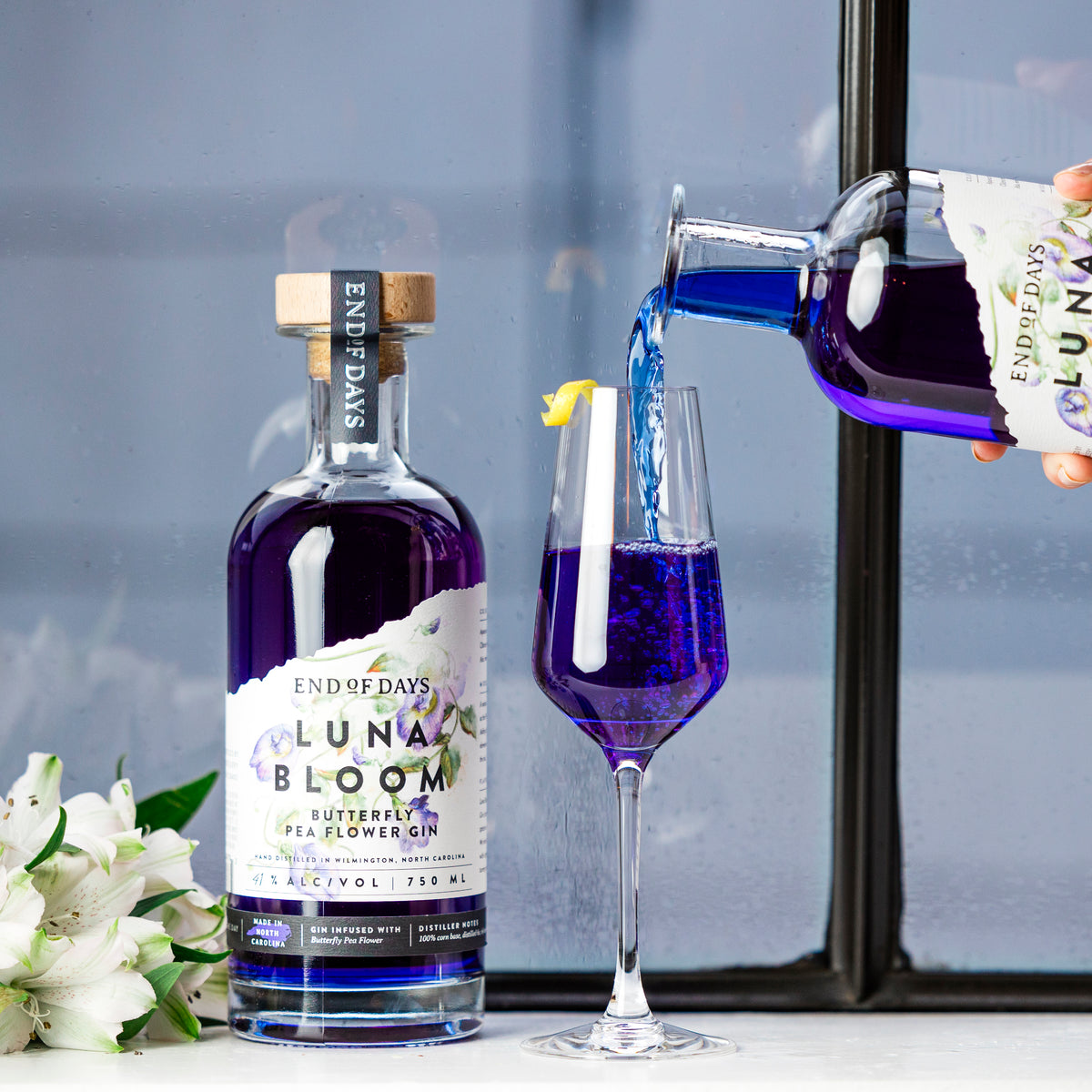 Luna Bloom Butterfly Pea Flower Gin being poured into a flute glass beside the bottle