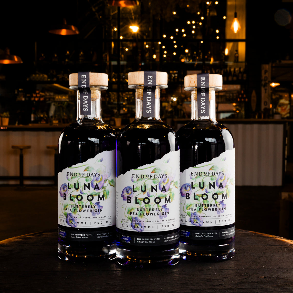 Three bottles of Luna Bloom purple gin lined up on a table, labels facing forward