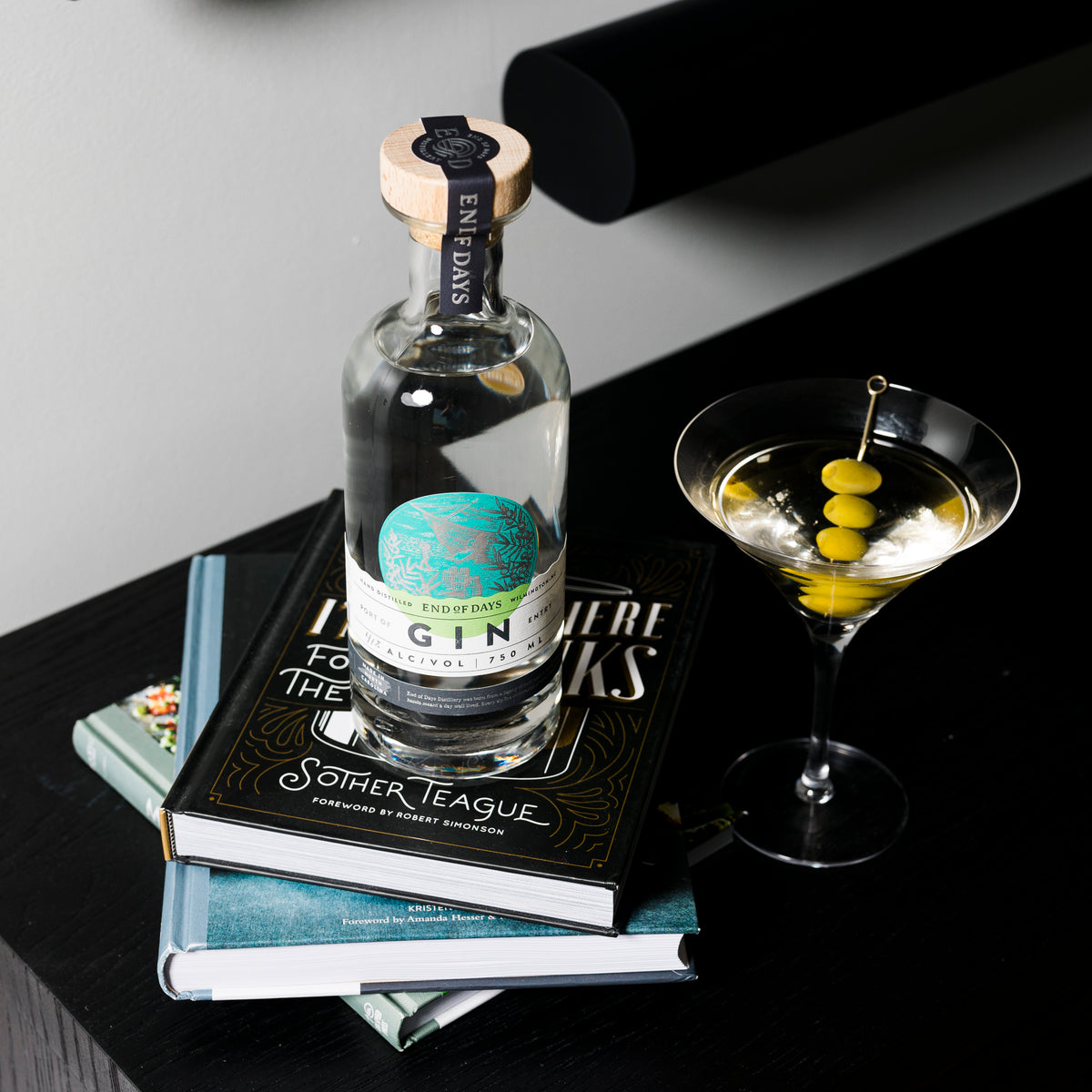 Port of Entry Gin bottle on a stack of books beside a classic gin martini with olives