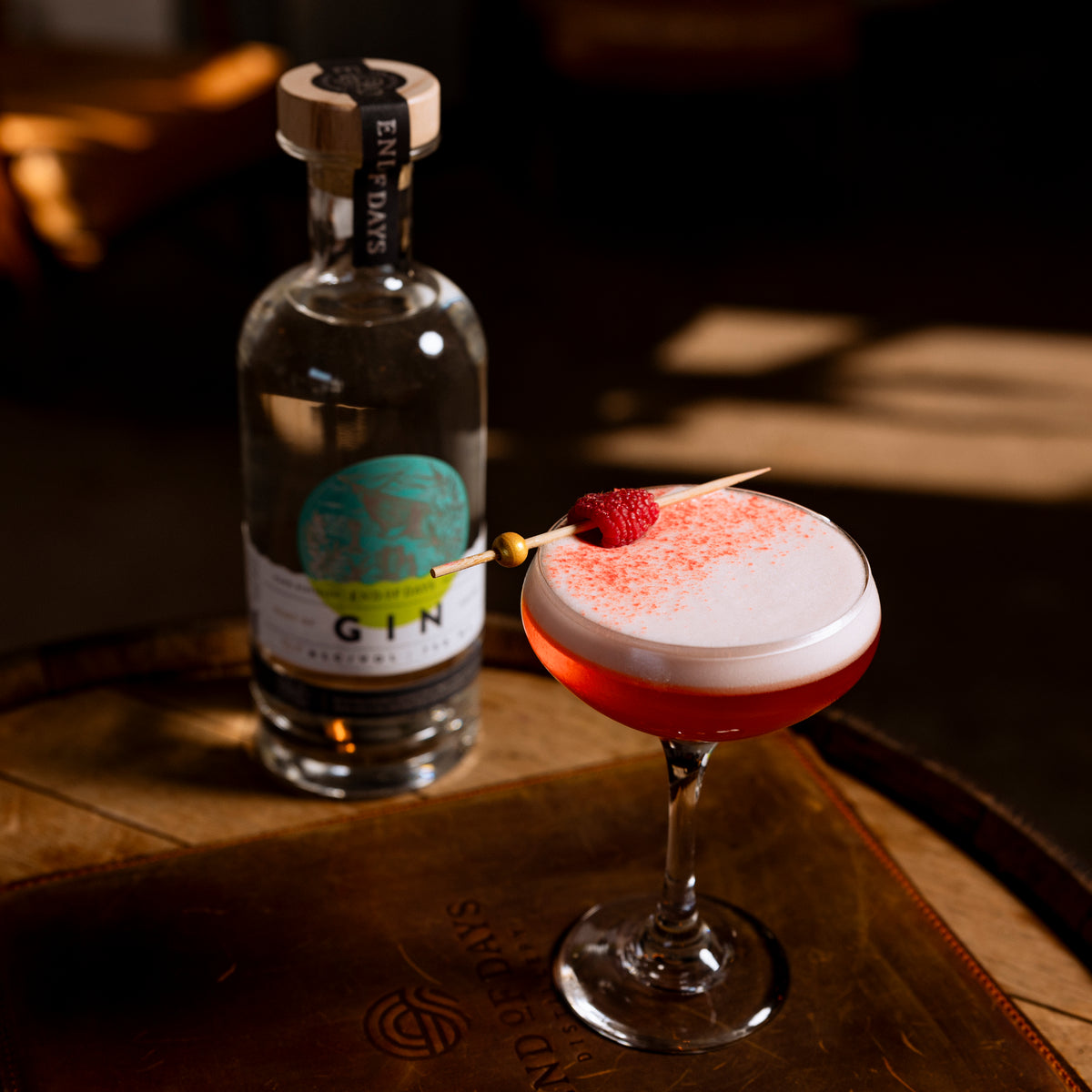 Port of Entry Gin bottle beside a frothy pink gin sour cocktail on a barrel top
