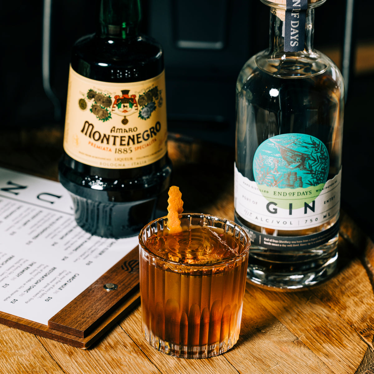Port of Entry Gin bottle beside a stirred amber gin cocktail with an orange twist on a bar menu
